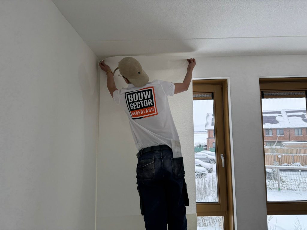 Behanger zet een baan vlies bovenaan tegen de muur vast bij het plafond