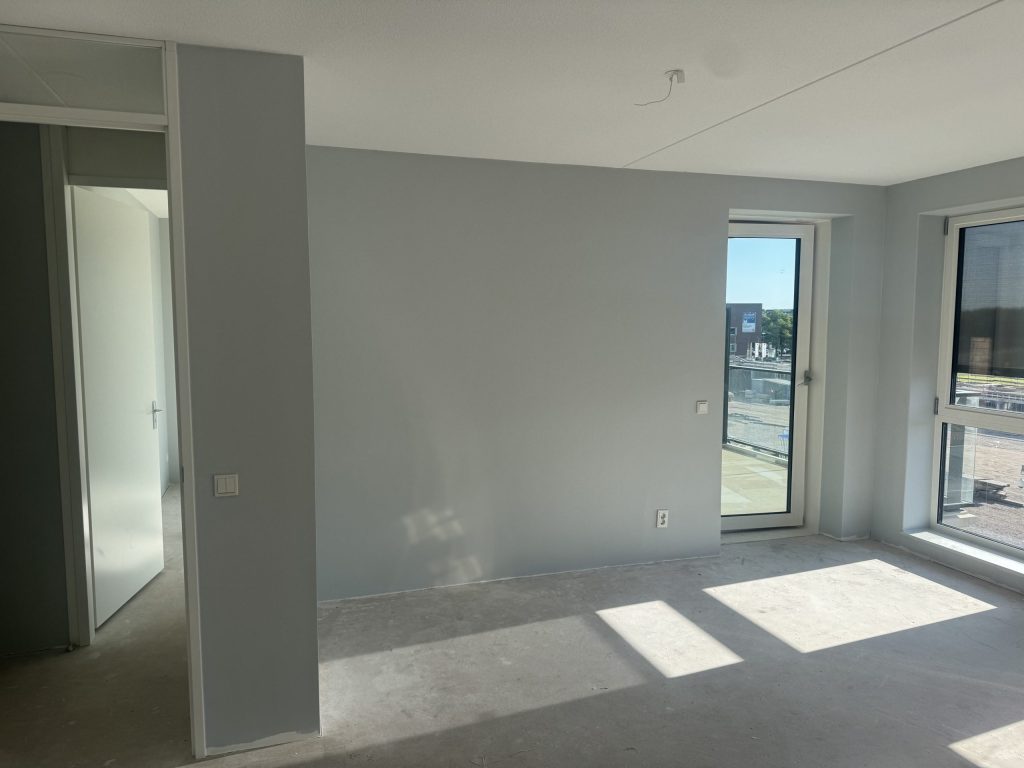 Kamer in een appartement met lichtgrijs gesausde wanden en een balkondeur