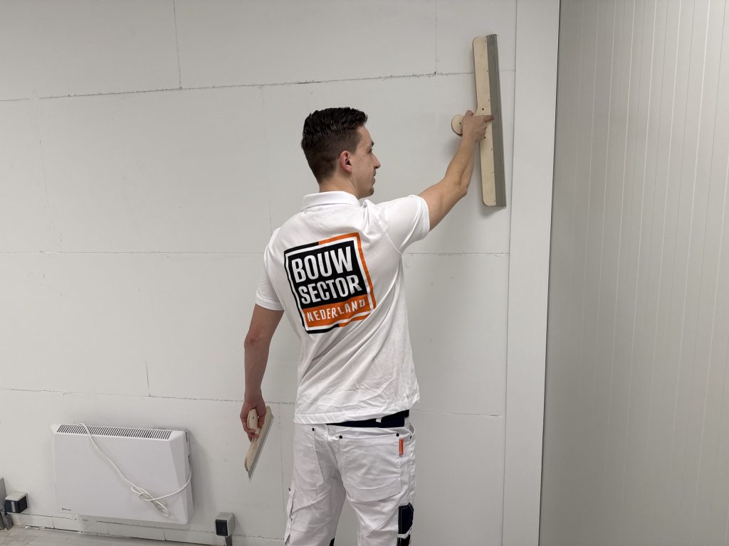 Vakman van Bouwsector Nederland trekt een muur vlak met een spaan voordat er behang op gaat